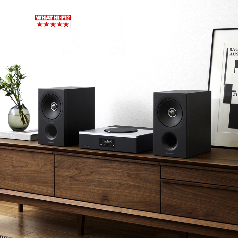 A pair of black speakers and a central unit placed on a wooden cabinet. 