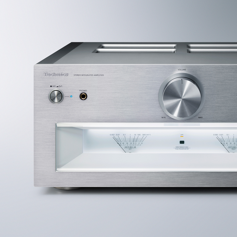 A close-up of a silver audio receiver or amplifier, showing a large volume knob and several buttons.