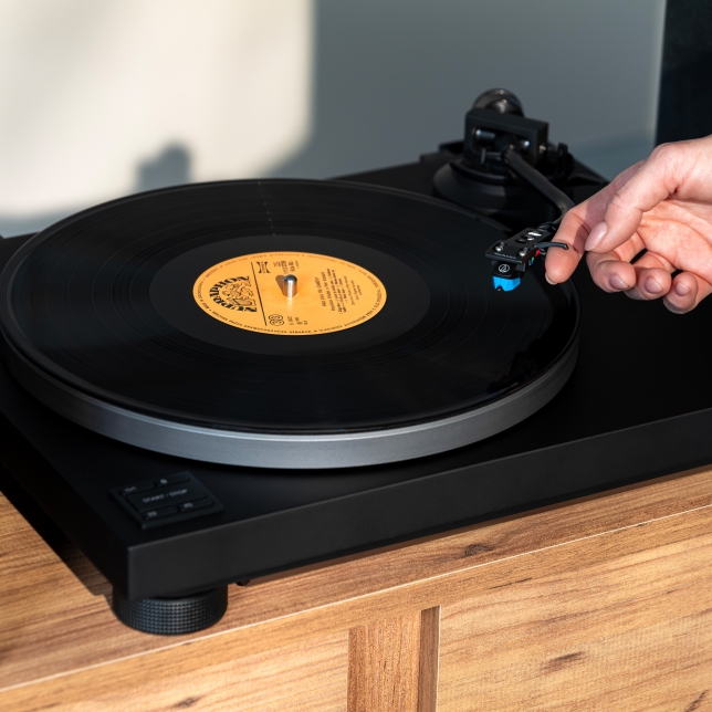 Details of the Technics SL-40CBT turntable in a stylish living room, in Black colour. We can see a hand operating the cartridge.