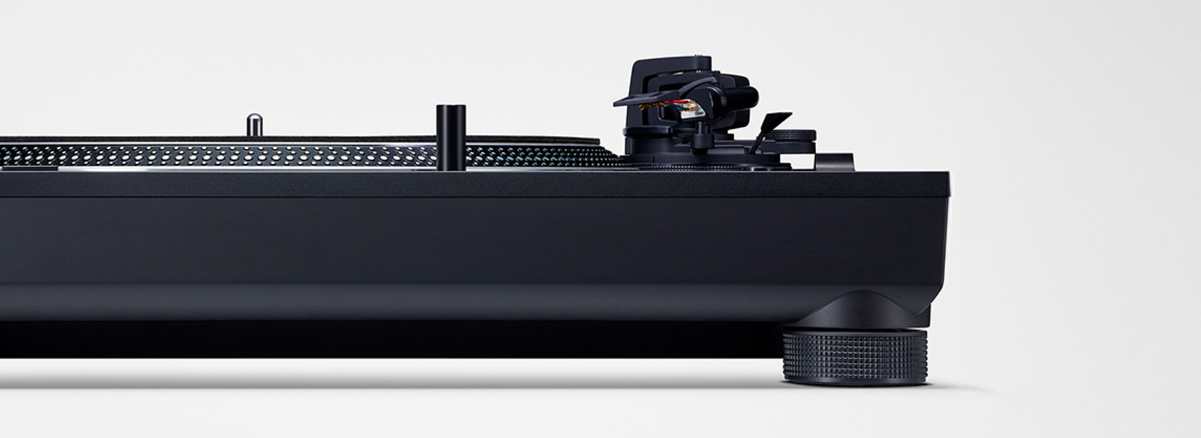 This image shows a side profile of a turntable, highlighting the platter edge, tonearm assembly, and a textured isolation foot (insulator) designed to reduce vibration under the matte black base.