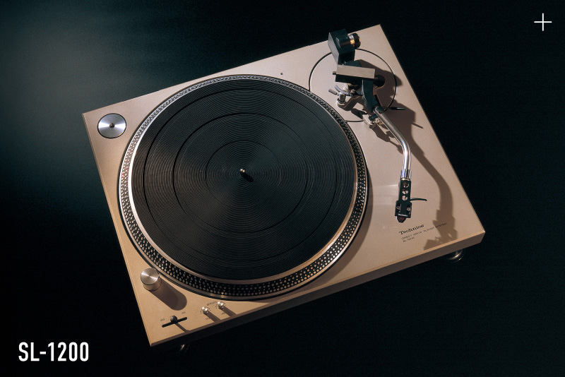 Photograph of the Technics SL-1200 turntable in gold finish, shot from above against a dark background, with the model name "SL-1200" displayed in the lower left.