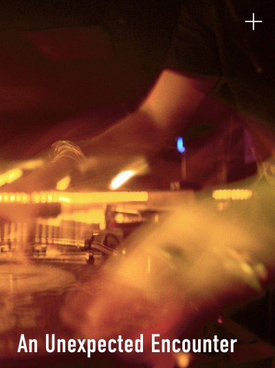 A close-up, motion-blurred photograph of a DJ performing on turntables under warm stage lighting, with the caption "An Unexpected Encounter" in white text at the bottom.