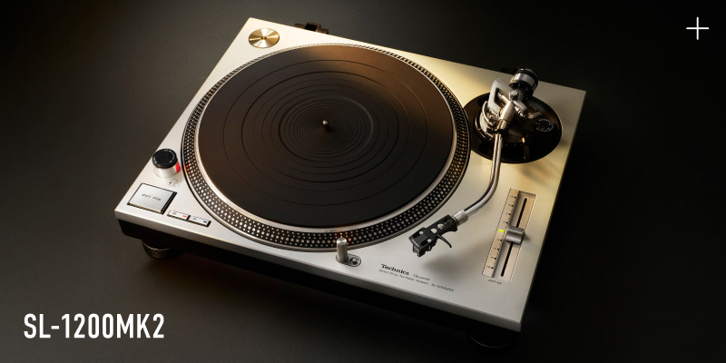 Photograph of the Technics SL-1200MK2 turntable in silver finish, shot from above against a dark background, with the model name "SL-1200MK2" displayed in the lower left.