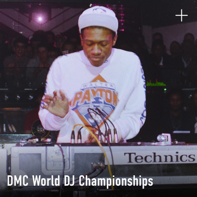 A photograph of a DJ performing on Technics turntables at the DMC World DJ Championships, wearing a Walter Payton jersey, with the Technics logo visible on the equipment.
