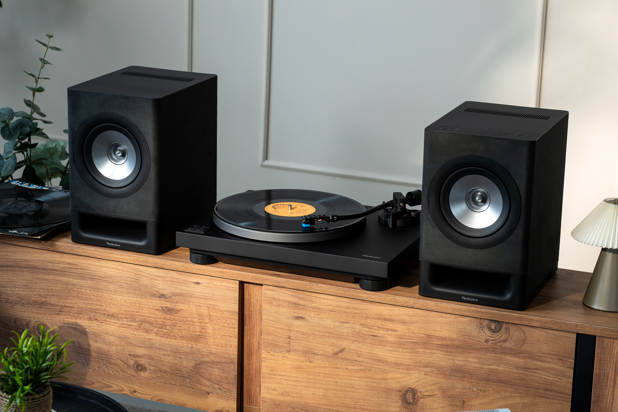 Les enceintes sans fil CX700 et la platine 40CBT de Technics s’intègrent avec élégance sur un meuble en bois, au cœur d’un salon à la décoration soignée. Les deux produits sont présentés en finition noire.